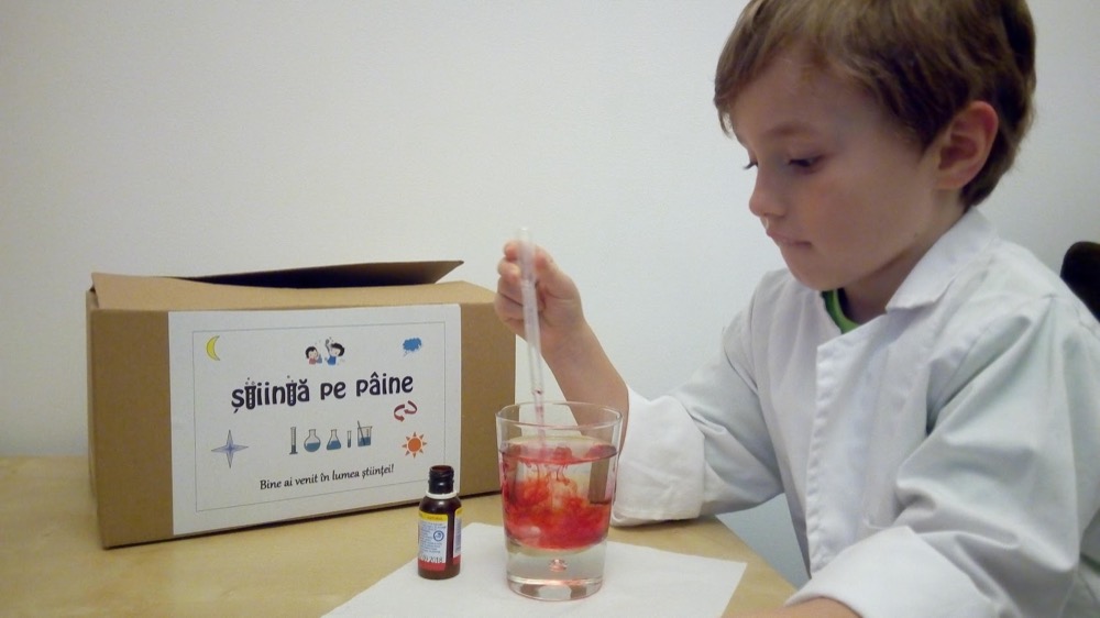 Băiat în halat care face un experiment lângă cutia Știință pe pâine