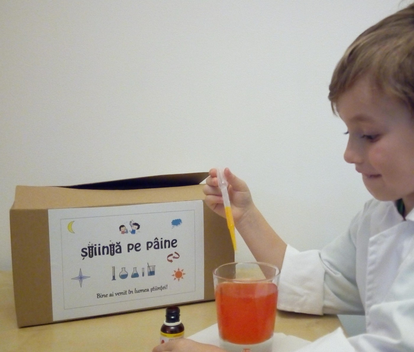 Copil în halat care face un experiment lângă cutia Știință pe pâine